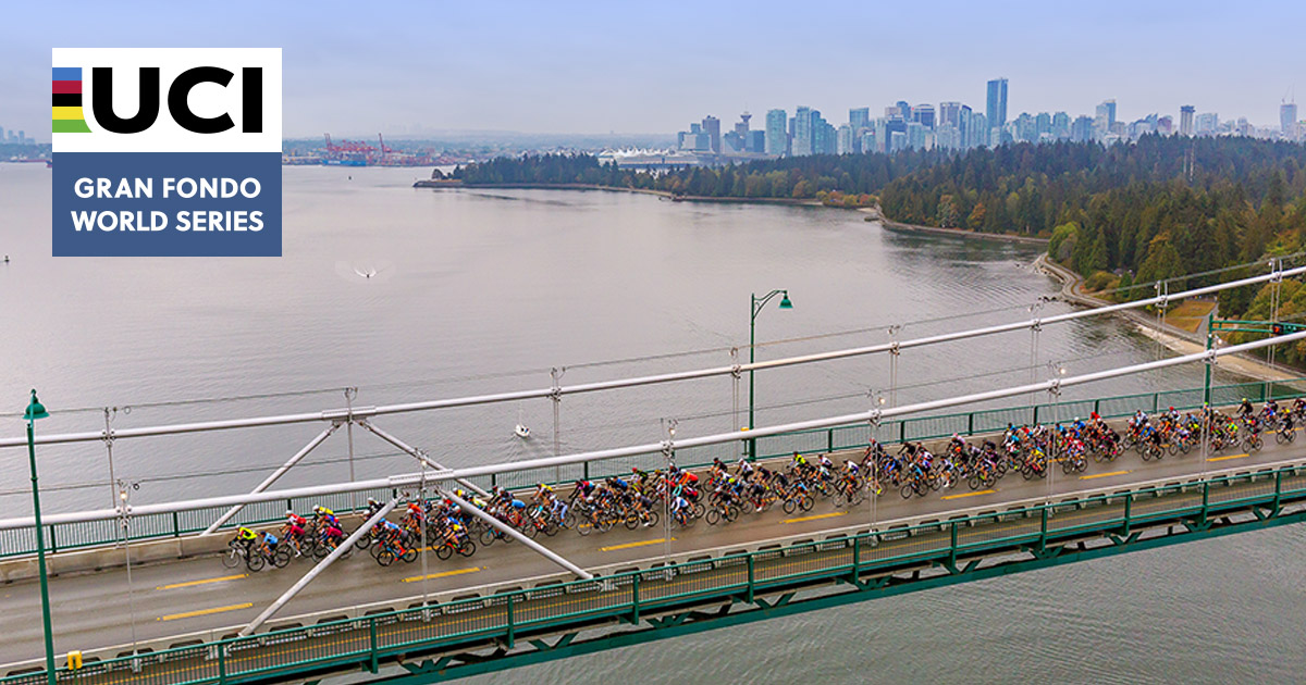 A large group of cyclists cross the Lions Gate bridge with Vancouver and Stanley Park in the background with UCI Gran Fondo World Series logo